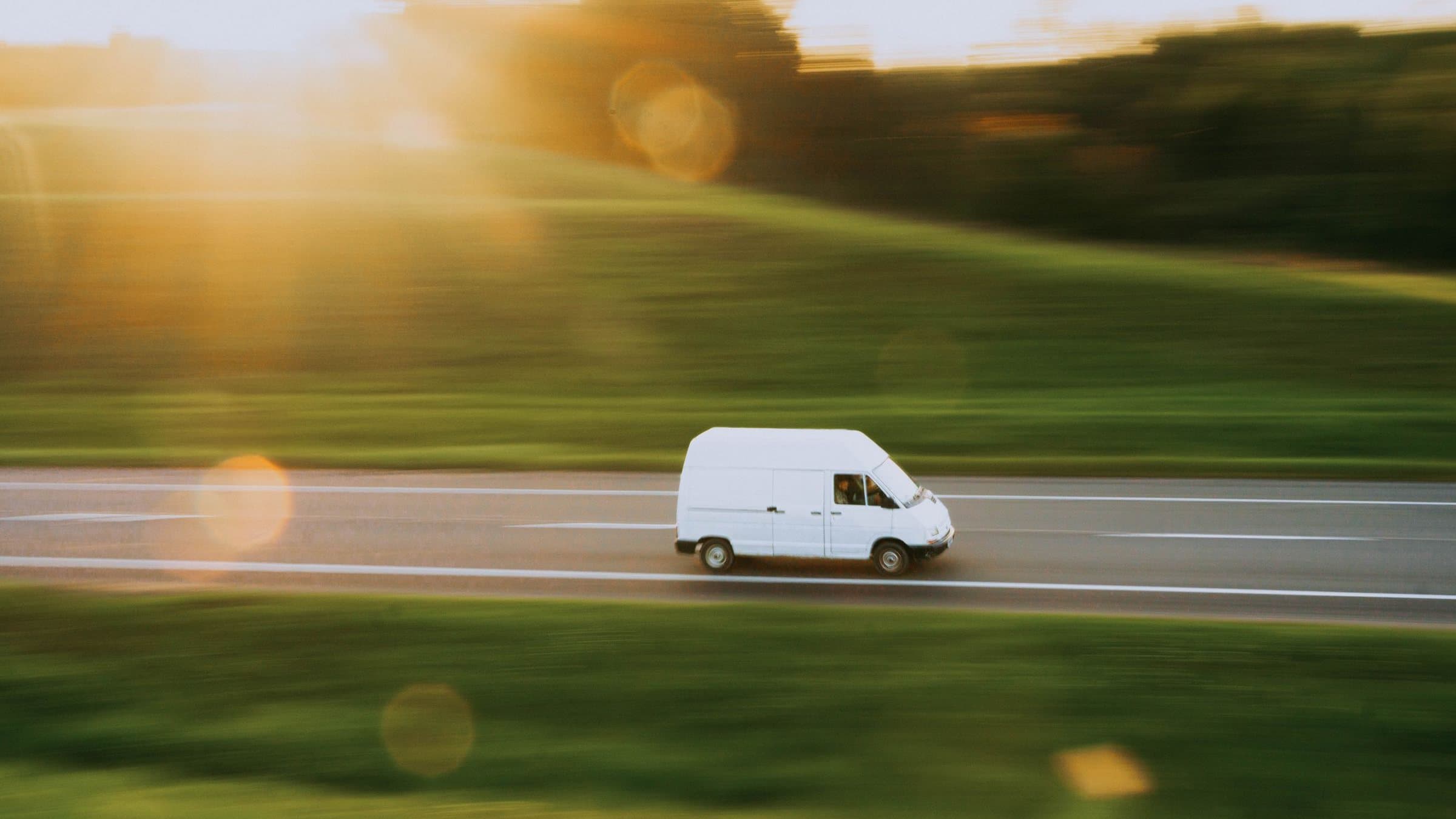 夕暮れの道を走る軽貨物車